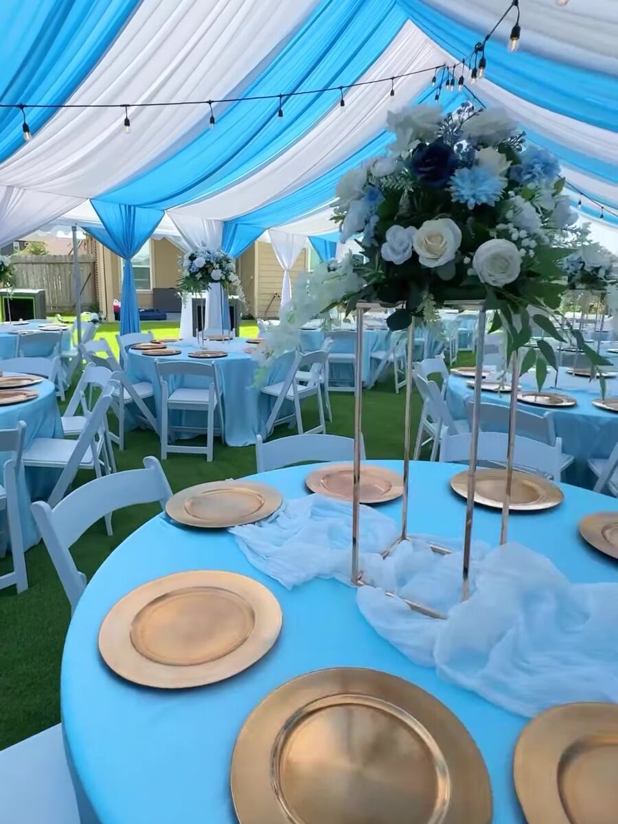 Blue and white draped tent ceiling above a round table with gold chargers and a tall floral centerpiece