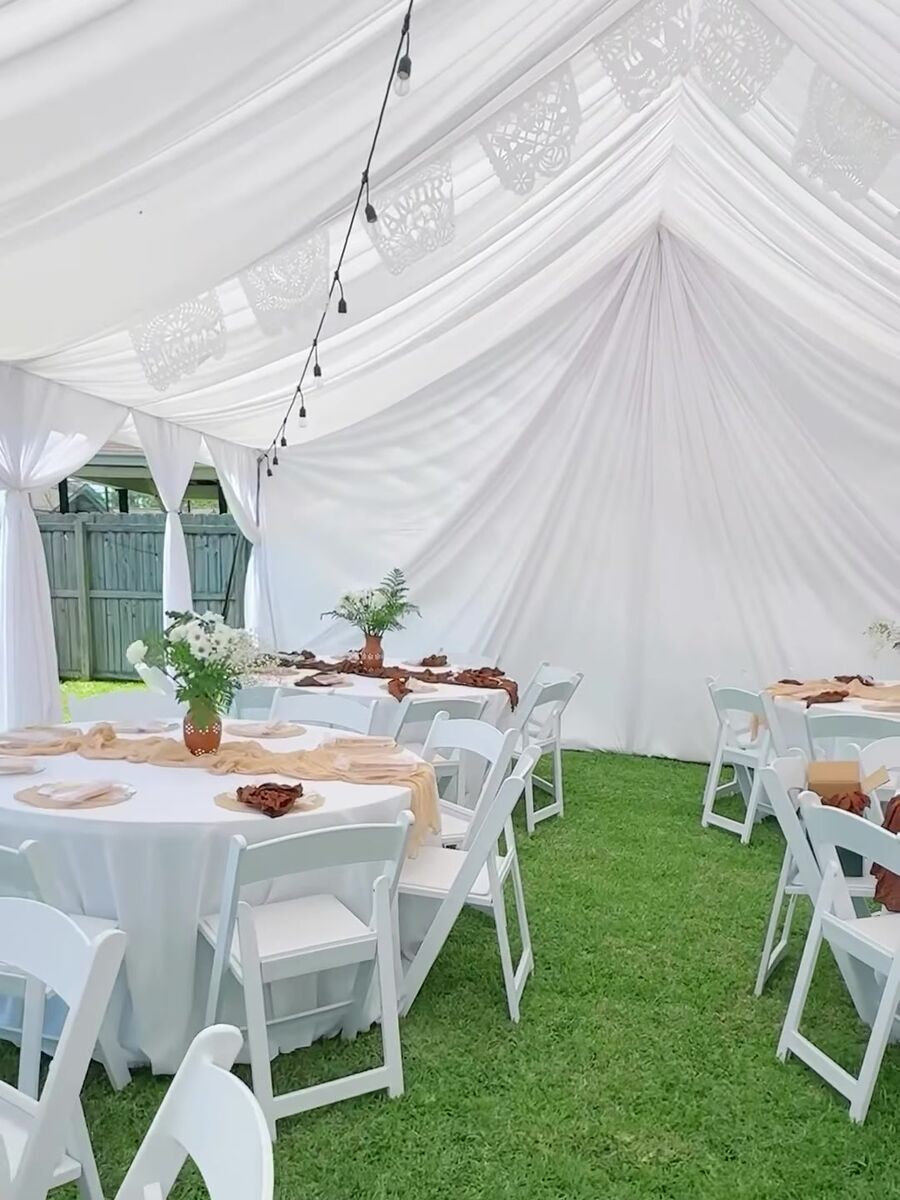 White draped tent ceiling with string lights over round tables on a lawn