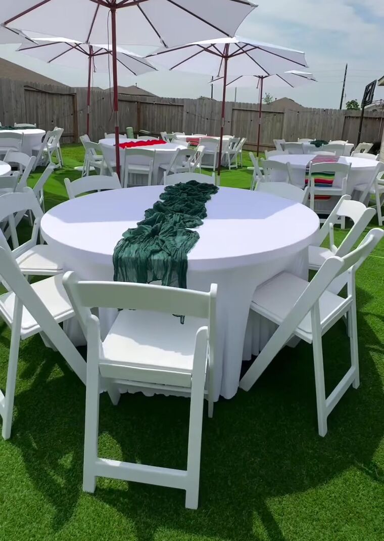Round table with a green runner and white chairs under umbrellas