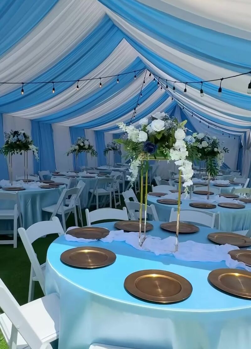 Tent draped in blue and white with round tables, gold chargers and tall floral centerpieces