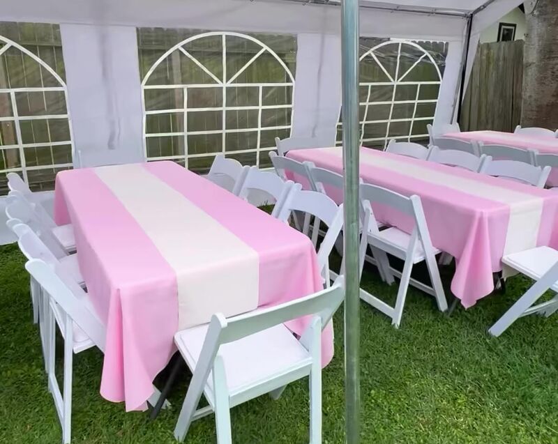 Tables with pink covers and white chairs under a tent with window walls