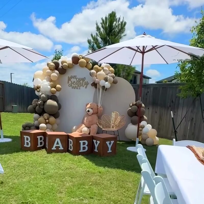 Baby shower backdrop with balloons beside white umbrellas and tables