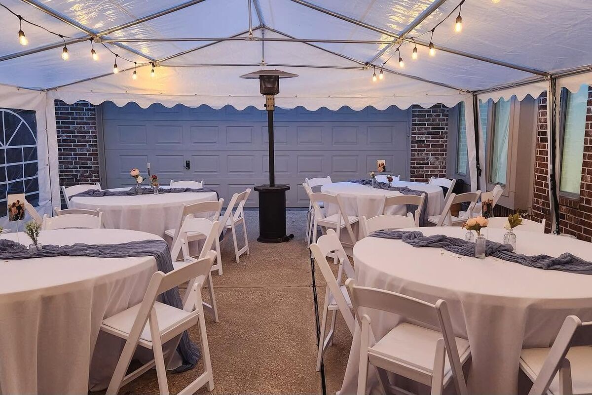 Round tables with white linens and white chairs under a tent with string lights
