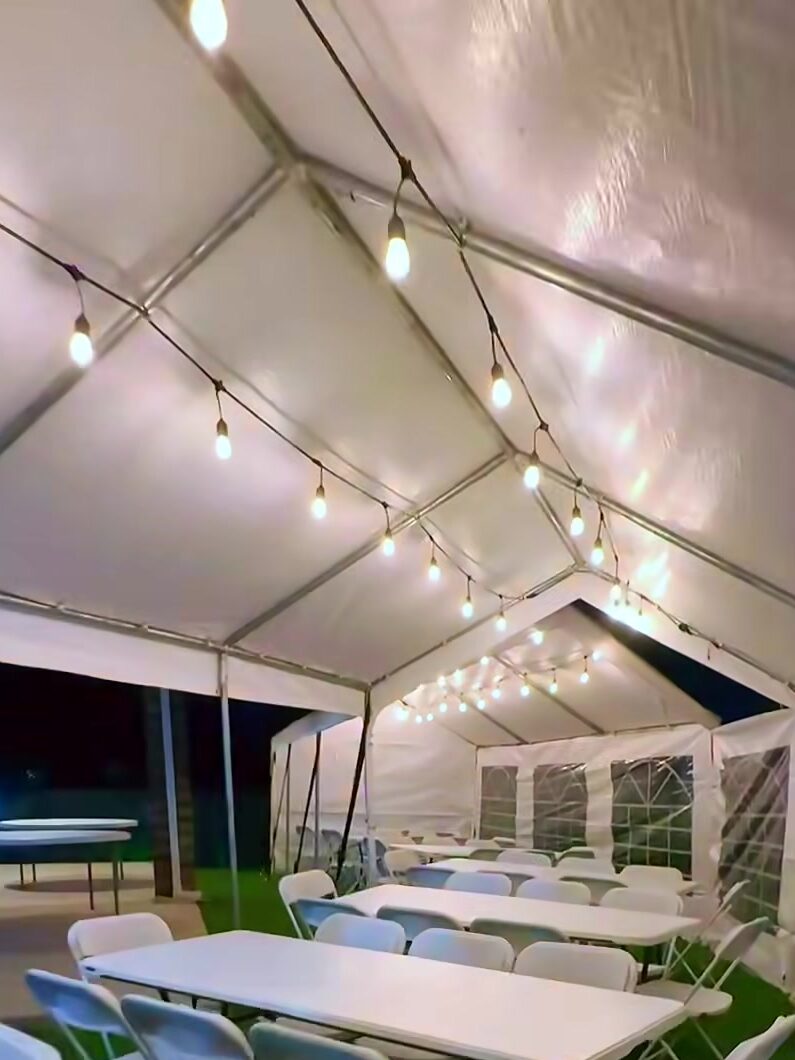 Tent lit with string lights at night over rows of tables and chairs
