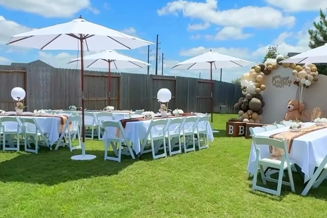 White market umbrellas shading rows of tables on a lawn under a blue sky